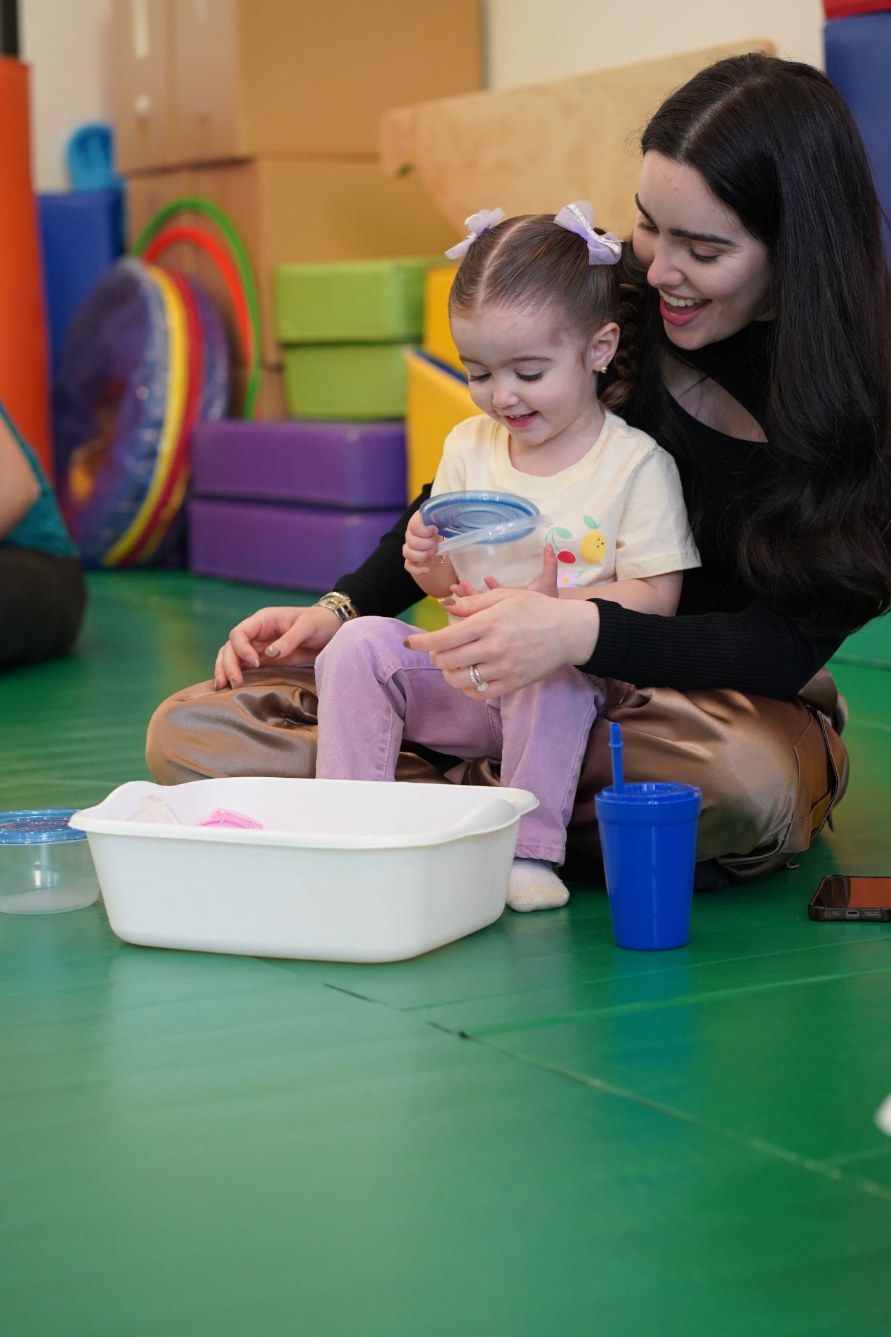 Maestra y niña jugando con contenedores sobre un tapete verde