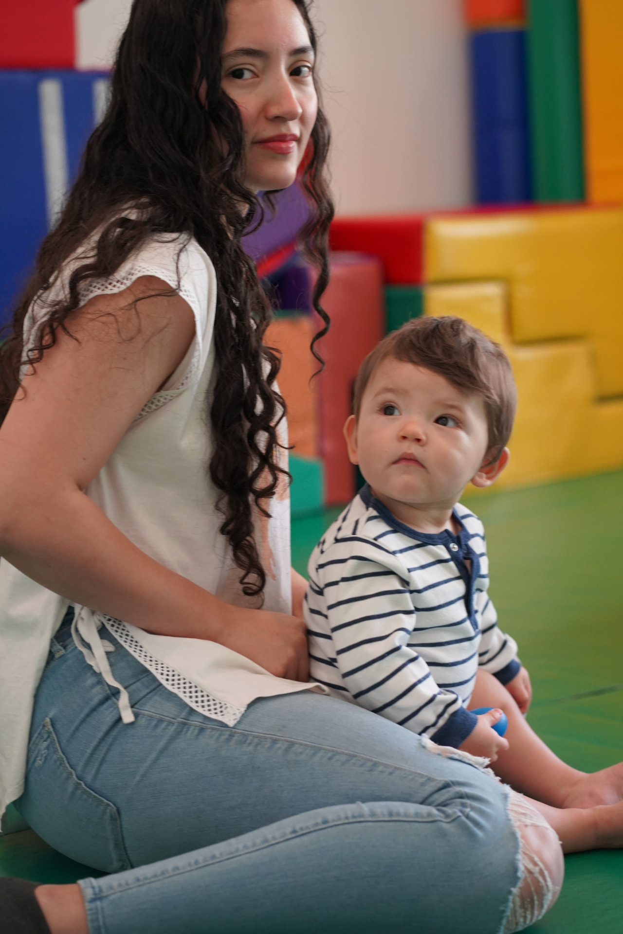 Bebé sentado junto a su maestra en el área de juego
